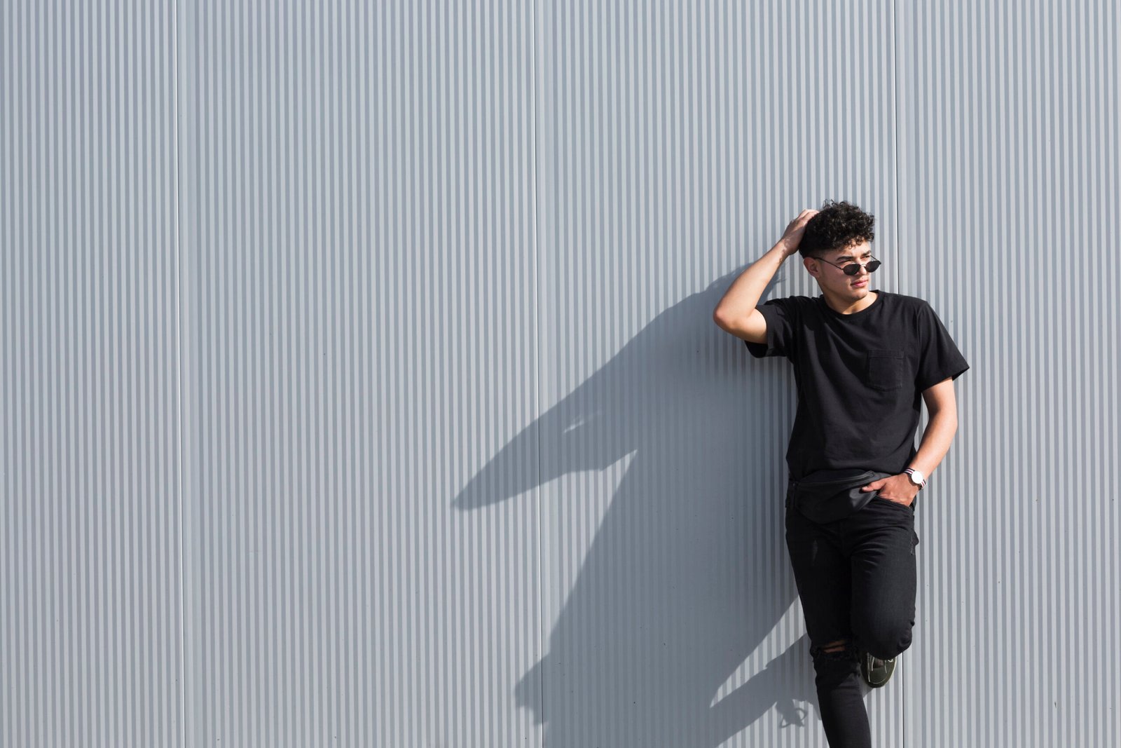 Model wearing a black T-shirt and black jeans against a grey wall